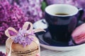 Cup of black coffee, lilac flowers and sweet pastel french macaroons on light wooden table