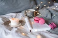 Cup of black coffee with paper book and burning candle with pink tasty macarons cookies in bed close up.