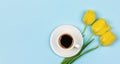A Cup of black coffee on a saucer and a bouquet flowers yellow tulips on a blue background with copy space. Royalty Free Stock Photo