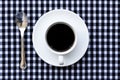 A Cup of Black Coffee and Shining Spoon on Black and White Plaid Fabric Background