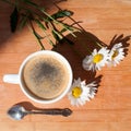 A cup of black coffee, silver spoon, branch of white daisy flowers on wooden background top view Royalty Free Stock Photo