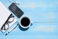 Cup of black coffee and smart phone with office supplies; pen, notebook and eyes glasses on blue wooden table background Royalty Free Stock Photo