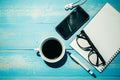 Cup of black coffee and smart phone with office supplies; pen, notebook and eyes glasses on wooden table background Royalty Free Stock Photo