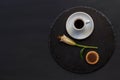 Cup of black coffee tea, cookie with chocolate, single bud of lily flower on a round slate on a black background