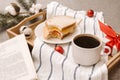 Cup of black coffee on a tray, gift box with red ribbon, open book, red balls, sandwich on a saucer, fir and cotton branches