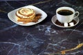 A cup of black coffee with two pieces of sugar in a saucer and a plate with a bun in the glaze with cinnamon sticks and star anise Royalty Free Stock Photo