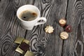 A cup of black coffee in a white cup. Chocolate in foil and chocolates. On pine boards