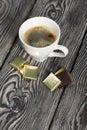 A cup of black coffee in a white cup. Chocolate in foil. On pine boards