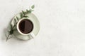 Cup of black coffee on a white textured table with a branch of eucalyptus