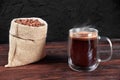 A cup of black coffee on wooden table. A glass mug of coffee. Coffee beans in bag on wooden background. Morning coffee Royalty Free Stock Photo