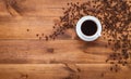 Cup of black morning coffee and cofee beans scattered on brown wooden table, espresso dark coffe aroma cafe shop background, warm Royalty Free Stock Photo