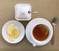 Cup of black tea and lemons on plate and sugar on gold fabric