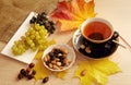 Cup of black tea, nuts, black and white grapes, red and yellow leaves, dried canker berry