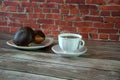 A cup of black tea on a saucer and a plate with two donuts in chocolate icing lie on a wooden table against a brick wall. Close-up Royalty Free Stock Photo