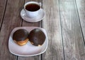 A cup of black tea on a saucer and a plate with two donuts in chocolate icing lie on a wooden table. Close-up Royalty Free Stock Photo