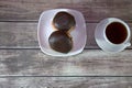 A cup of black tea on a saucer and a plate with two donuts in chocolate icing lie on a wooden table. Close-up Royalty Free Stock Photo