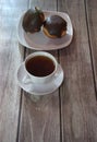 A cup of black tea on a saucer and a plate with two donuts in chocolate icing lie on a wooden table. Close-up Royalty Free Stock Photo