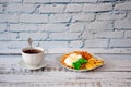 A cup of black tea on a saucer with a spoon and a plate of waffles with cream and banana pieces