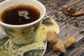 A Cup of black tea, tea leaves in a wooden spoon, pieces of brown sugar on a wooden background. Close up Royalty Free Stock Photo