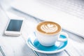 Cup of cappuccino art coffee smartphone and white laptop