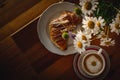 Cup of cappuccino coffee and croissant / brioche on a wooden table with freshly gathered daisy flowers. Italian breakfast. Royalty Free Stock Photo