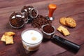 Cup of cappuccino, crackers, cookies, holder with ground coffee, tamper and cans of coffee beans on wooden table Royalty Free Stock Photo