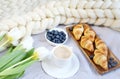 Cup with cappuccino and croissants, berries, white pastel giant knit blanket