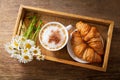 Cup of cappuccino , croissants and daisy flowers on a wooden tray