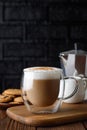 cup of cappuccino and geyser coffee maker on wooden table with black brick wall as background Royalty Free Stock Photo