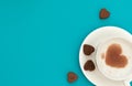 The cup of cappuccino with heart-shaped cocao on coffee foam and chocolate hearts on blue background. Valentine`s Day concept. Royalty Free Stock Photo