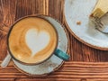Cup of cappuccino with latte art and a cheesecake near it on a brown wooden background. Stylish foam, retro cup of coffee in a cof Royalty Free Stock Photo
