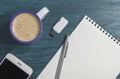 Cup of cappuccino, paper notepad, pen, smartphone and flash drive on the wooden background.