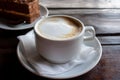 Cup of cappuccino and piece of cake on black wooden table. Cup of coffee with milk foam and dessert on dark background. Royalty Free Stock Photo