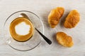 Cup with cappuccino, spoon on saucer, small croissants on wooden table. Top view