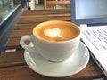Cup of cappuccino and white laptop on wooden cafe table Royalty Free Stock Photo