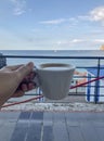 A cup of cappuccino in woman`s hands close-up across sea view. Coffee on the beach. Vertical. Travel. Vacation