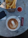 A cup of cappucino coffee with a basket of french fried on the table