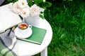 Cup of chamomile herbal tea with chamomile flower mint and teapot with flowers roses, books, warm plaid on white table outdoor.