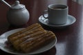 A cup with chocolate and milk and a plate with some traditional spanish churros.