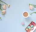 Cup of cocoa, macaroons cookies colorful in pastel colors and delicate pink ranunculus flowers on a pale blue background