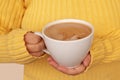 Cup of cocoa with milk or cappuccino in the hands of a girl in a yellow sweater, the concept of autumn mood, close-up Royalty Free Stock Photo