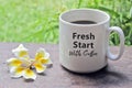 A cup of coffee with Bali frangipani flower on the wooden table with inspirational quote on it - Fresh start with coffee.