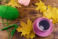 Cup of coffee, ball of yarn, knitting, knitted scarf and yellow maple leaves on wooden table. Autumn still life