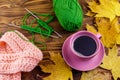 Cup of coffee, ball of yarn, knitting, knitted scarf and yellow maple leaves on wooden table