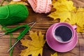 Cup of coffee, ball of yarn, knitting, knitted scarf and yellow maple leaves on wooden table. Autumn still life