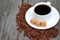 A cup of coffee with coffee beans and cane sugar on a wooden background. White coffee cup and saucer Royalty Free Stock Photo