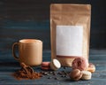 Cup of coffee, coffee beans, paper pack, macaroons and chocolate on wooden background