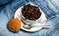 Cup with coffee beans, refined sugar and spoon on plate, denim background. Coffee break concept. Mug full of coffee Royalty Free Stock Photo