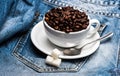 Cup with coffee beans, refined sugar and spoon on plate, denim background. Fresh brewed coffee concept. Mug full of Royalty Free Stock Photo