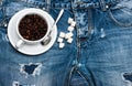 Cup with coffee beans, spoon and refined sugar lay on jeans near zip, denim background. Fresh brewed coffee concept. Mug Royalty Free Stock Photo